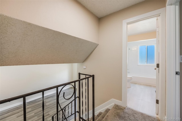 hall featuring an upstairs landing, a textured ceiling, and baseboards