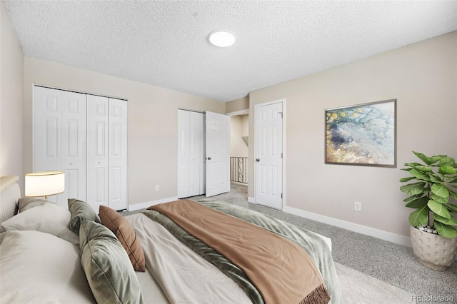 carpeted bedroom featuring a textured ceiling, baseboards, and multiple closets