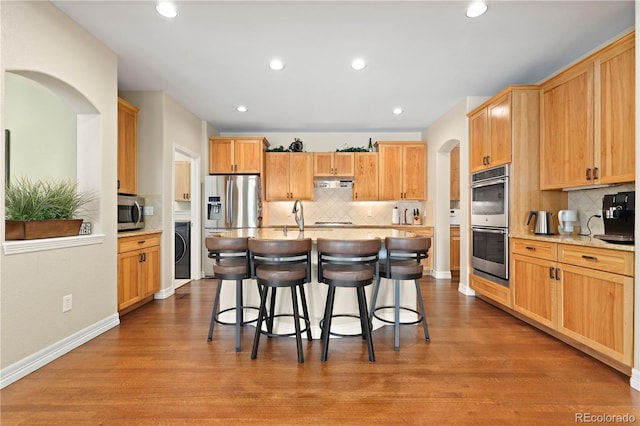 kitchen featuring washer / dryer, arched walkways, a kitchen breakfast bar, wood finished floors, and stainless steel appliances