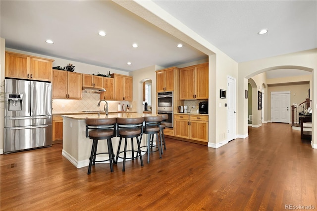 kitchen with appliances with stainless steel finishes, arched walkways, under cabinet range hood, and a kitchen breakfast bar