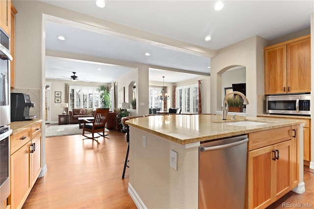 kitchen with light wood finished floors, stainless steel appliances, open floor plan, a kitchen island with sink, and a sink