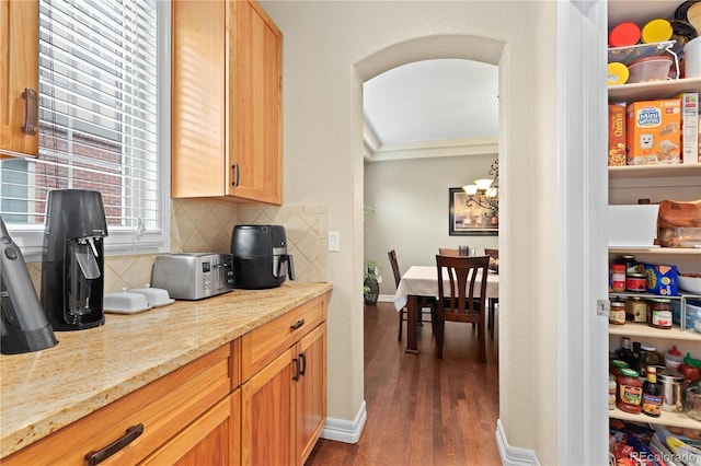 kitchen with arched walkways, a chandelier, light stone countertops, tasteful backsplash, and dark wood finished floors