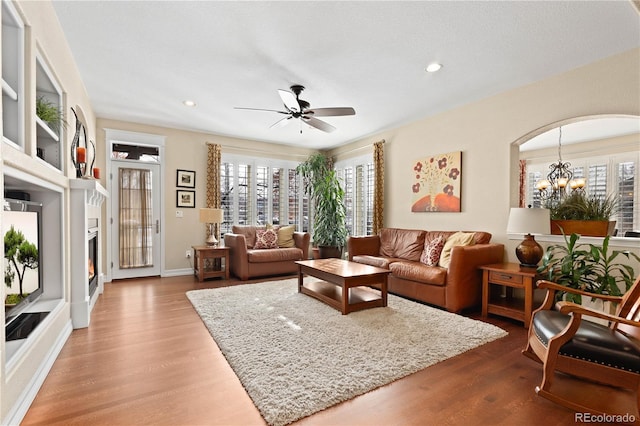 living area with arched walkways, recessed lighting, ceiling fan with notable chandelier, wood finished floors, and baseboards