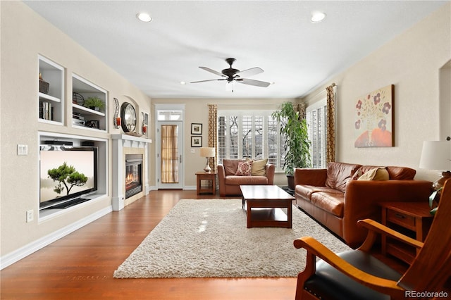 living room with baseboards, built in features, dark wood finished floors, and a glass covered fireplace