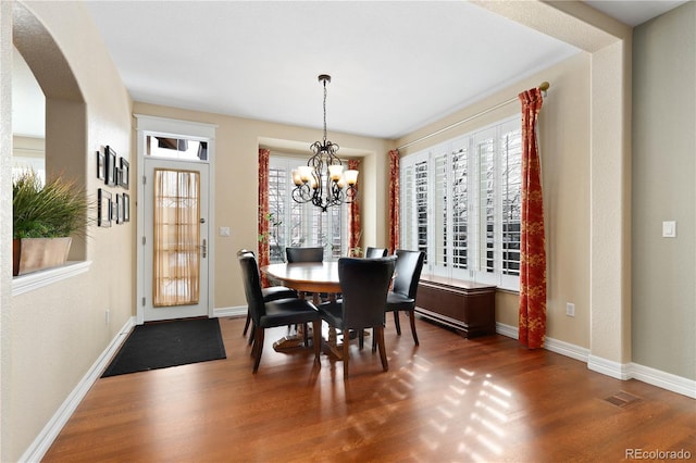 dining space featuring arched walkways, a notable chandelier, wood finished floors, and baseboards