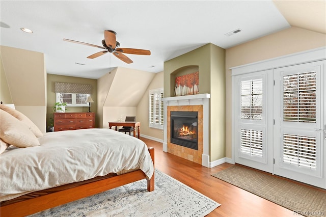 bedroom featuring access to exterior, lofted ceiling, visible vents, wood finished floors, and a tile fireplace