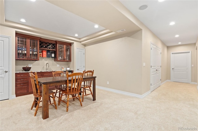 dining area with light carpet, baseboards, wet bar, and a tray ceiling