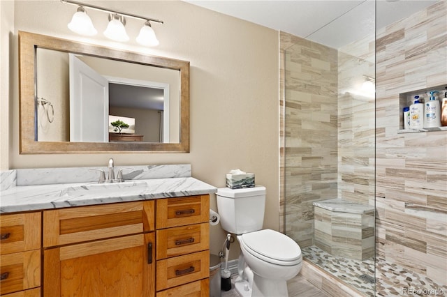 full bath with vanity, a tile shower, and toilet