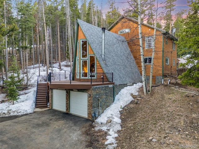 46 Apache Rd, Evergreen, CO 80439 - property exterior at dusk with roof with shingles, driveway, an attached garage, stairs, and a wooden deck