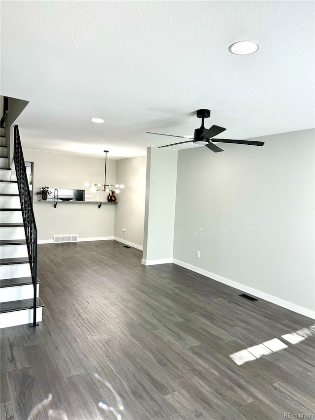 unfurnished living room featuring a textured ceiling, dark wood-type flooring, and ceiling fan with notable chandelier