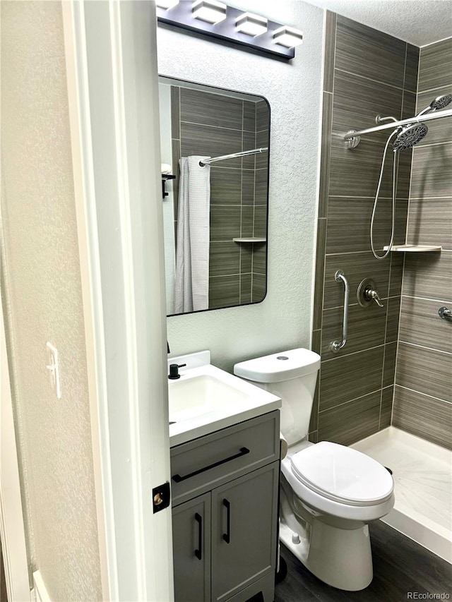 bathroom featuring hardwood / wood-style floors, vanity, toilet, and a tile shower