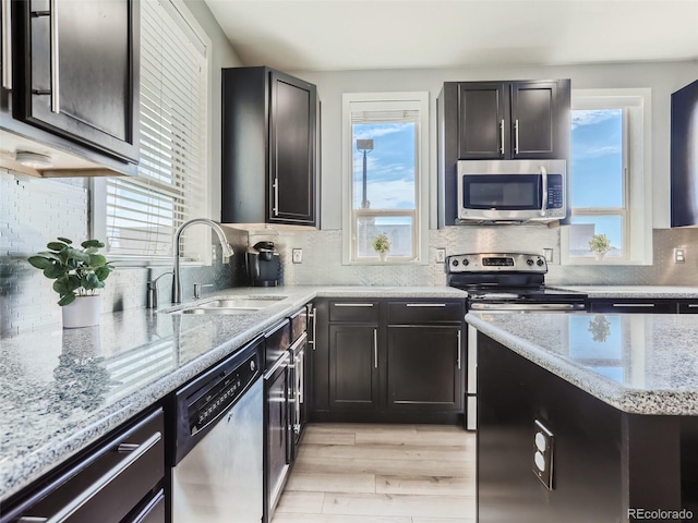 kitchen featuring sink, stainless steel appliances, light stone counters, backsplash, and light wood-type flooring