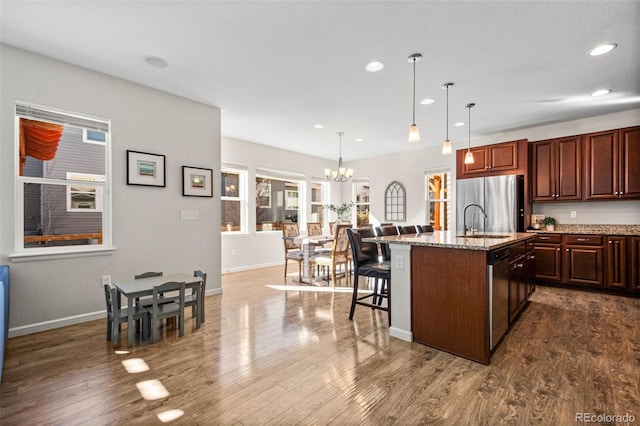 kitchen featuring a center island with sink, appliances with stainless steel finishes, a kitchen breakfast bar, dark hardwood / wood-style flooring, and pendant lighting