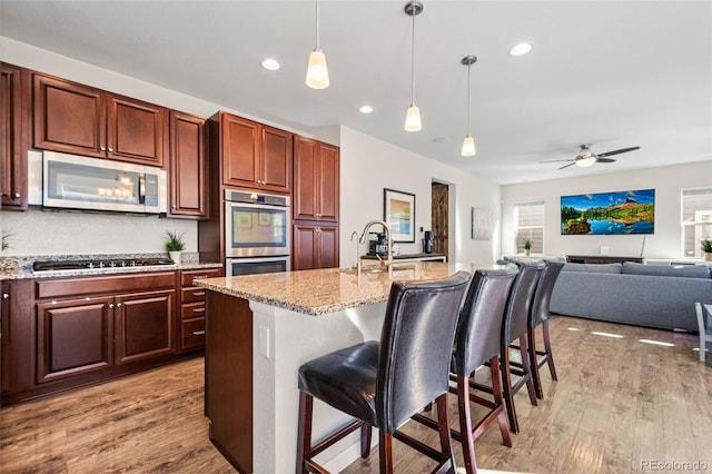 kitchen with appliances with stainless steel finishes, decorative light fixtures, a kitchen breakfast bar, a center island with sink, and light wood-type flooring