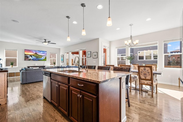 kitchen featuring a kitchen bar, sink, stainless steel dishwasher, light stone countertops, and a kitchen island with sink