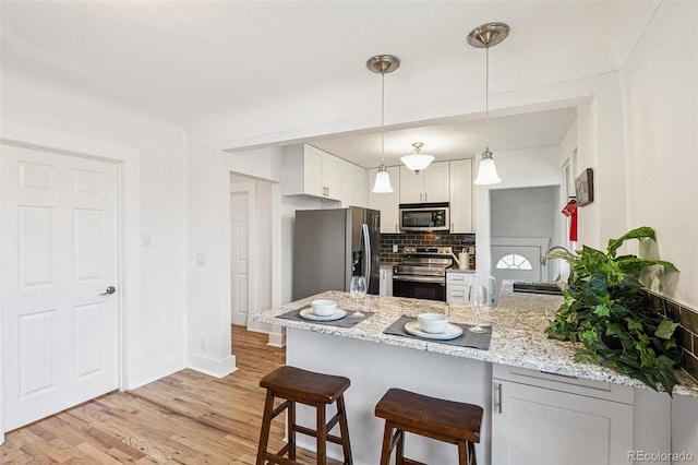 2800 N Fillmore St, Denver, CO 80205 - kitchen featuring stainless steel appliances, a peninsula, decorative backsplash, a breakfast bar, and light wood finished floors