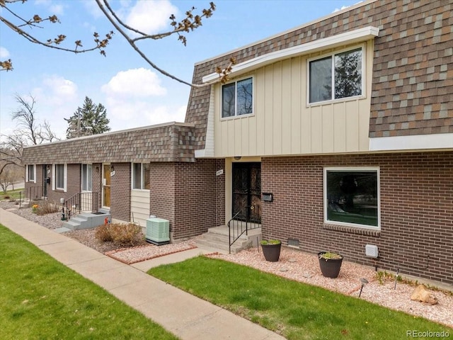 view of front of property with central air condition unit, mansard roof, a shingled roof, and brick siding