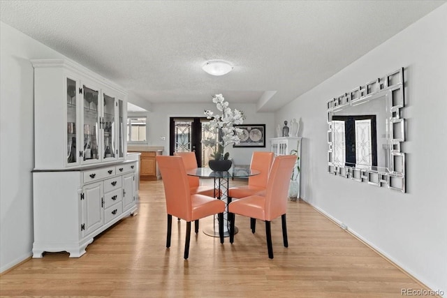 dining area featuring light wood-style flooring, a textured ceiling, and baseboards