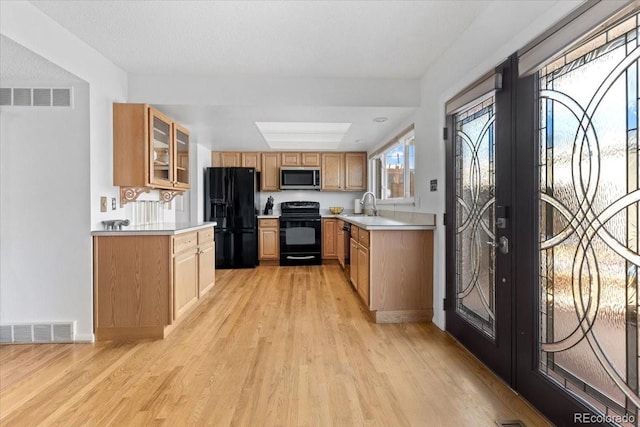 kitchen featuring visible vents, black appliances, a sink, light countertops, and light wood finished floors