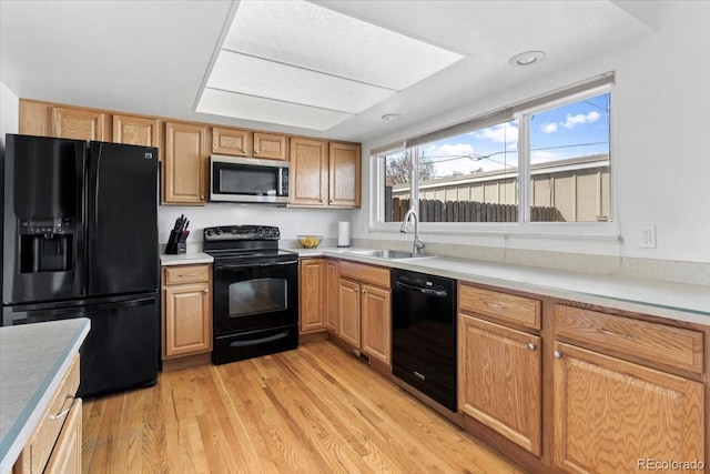 kitchen with a sink, light wood-type flooring, light countertops, and black appliances