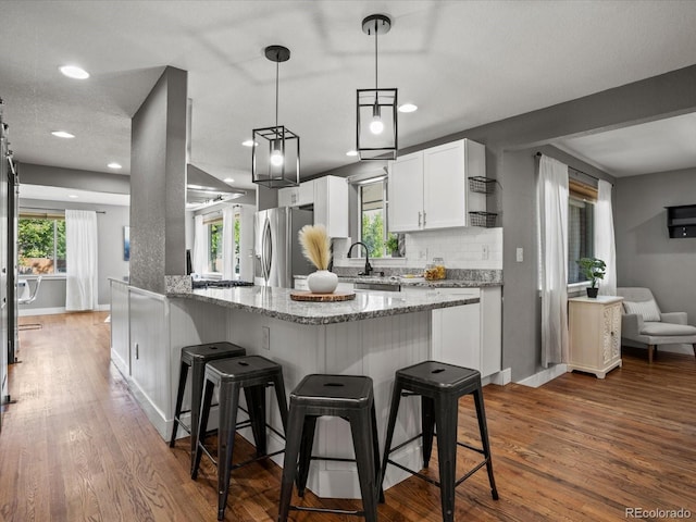 6943 Oak Way, Arvada, CO 80004 - kitchen featuring stainless steel refrigerator with ice dispenser, a breakfast bar area, light stone counters, white cabinets, and tasteful backsplash