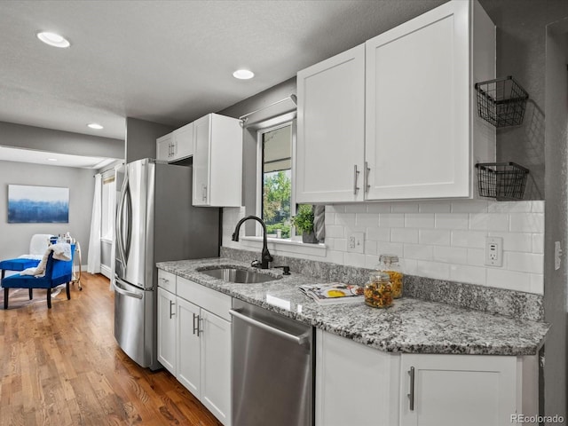 6943 Oak Way, Arvada, CO 80004 - kitchen featuring appliances with stainless steel finishes, white cabinets, tasteful backsplash, wood finished floors, and light stone countertops