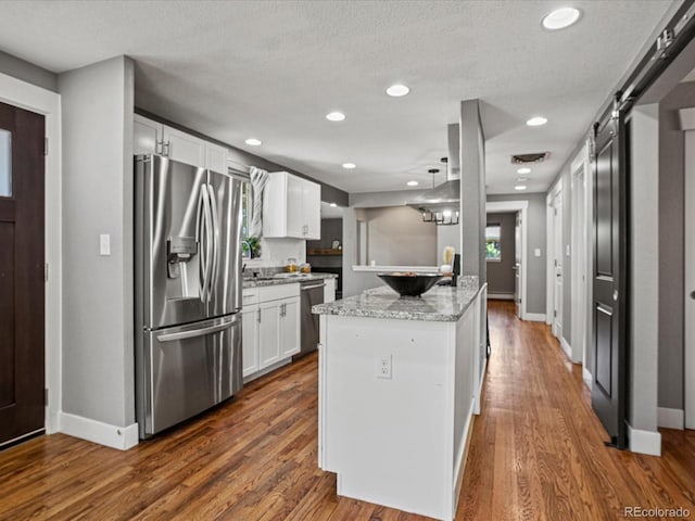 6943 Oak Way, Arvada, CO 80004 - kitchen featuring stainless steel appliances, white cabinetry, light stone counters, a barn door, and dark wood-type flooring