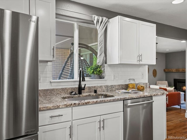 6943 Oak Way, Arvada, CO 80004 - kitchen featuring stainless steel appliances, a brick fireplace, white cabinets, decorative backsplash, and recessed lighting