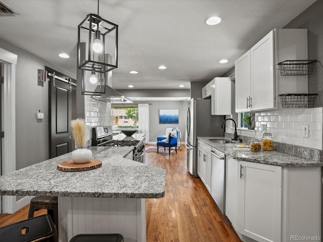 6943 Oak Way, Arvada, CO 80004 - kitchen with stainless steel appliances, white cabinetry, a breakfast bar area, backsplash, and light wood-type flooring