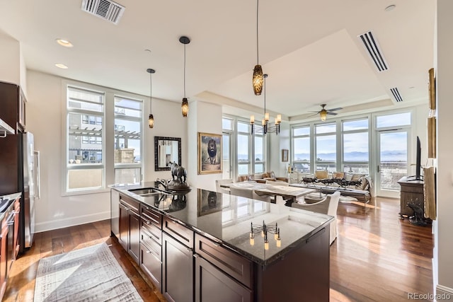 kitchen with hanging light fixtures, a kitchen island, dark brown cabinetry, and dark stone counters