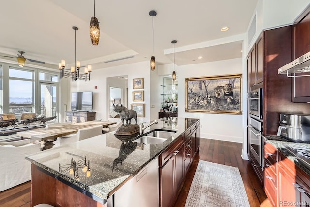 kitchen featuring sink, dark stone countertops, a center island with sink, dark hardwood / wood-style flooring, and decorative light fixtures