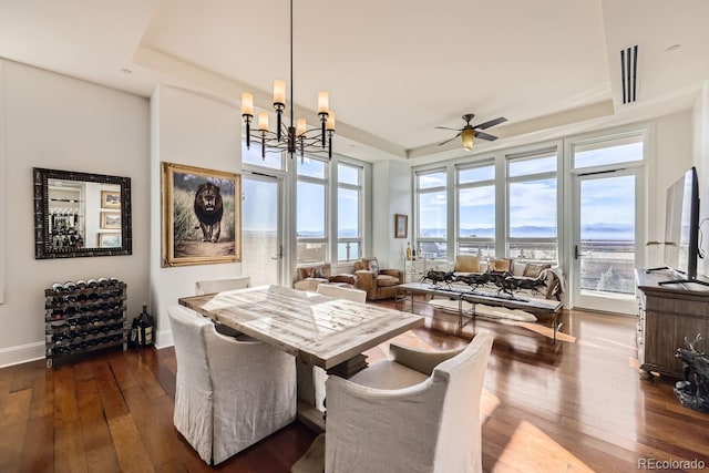 dining area with dark hardwood / wood-style floors, a tray ceiling, and ceiling fan with notable chandelier