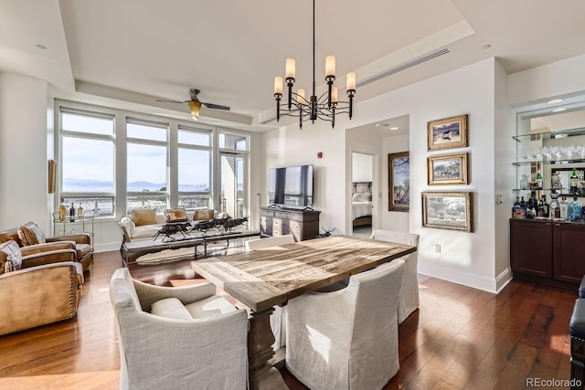 dining room with dark hardwood / wood-style floors, a raised ceiling, and ceiling fan with notable chandelier