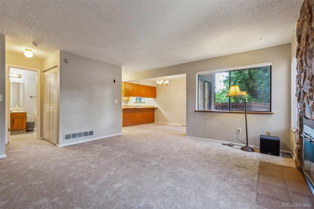 unfurnished living room with carpet, visible vents, a notable chandelier, and a textured ceiling