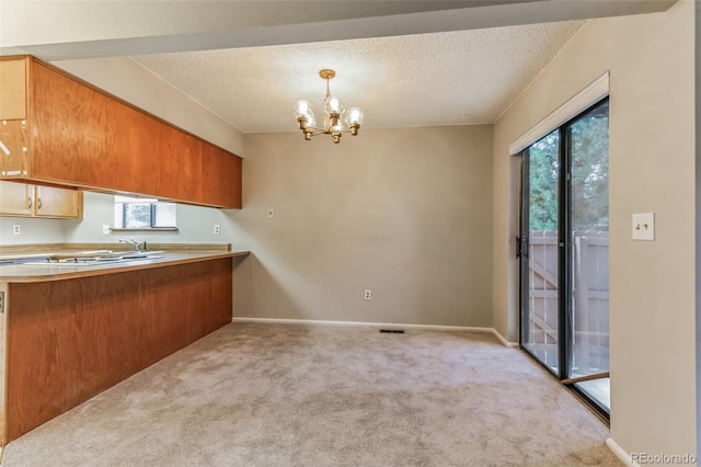 kitchen with light countertops, light carpet, a textured ceiling, a chandelier, and a peninsula