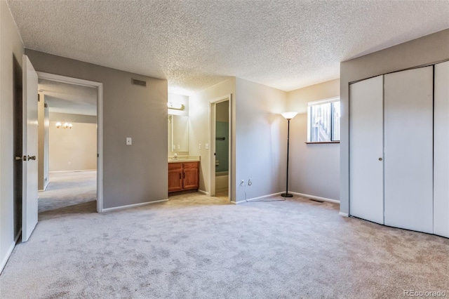 unfurnished bedroom featuring light carpet, visible vents, connected bathroom, a textured ceiling, and a closet