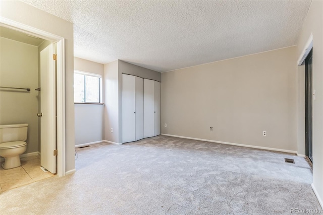 unfurnished bedroom with carpet floors, a textured ceiling, baseboards, and ensuite bathroom