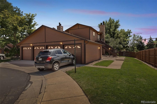 view of front facade featuring a chimney, concrete driveway, a lawn, fence, and a garage