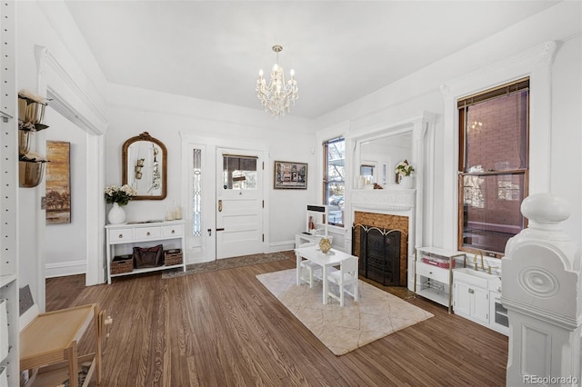 interior space featuring dark wood-type flooring, a brick fireplace, a notable chandelier, and baseboards