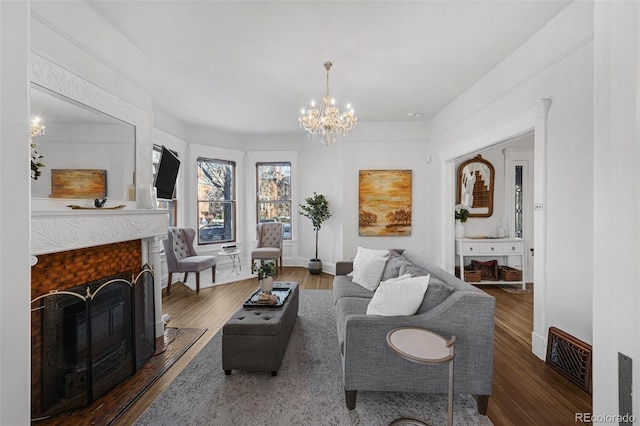 living room featuring a notable chandelier, visible vents, a fireplace with flush hearth, wood finished floors, and baseboards