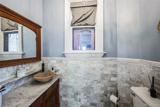 half bath featuring toilet, wainscoting, tile walls, and vanity