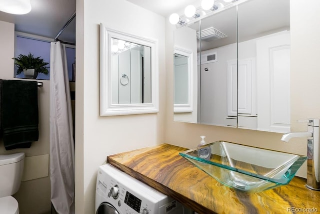 full bathroom with visible vents, a shower with shower curtain, toilet, vanity, and washer / dryer