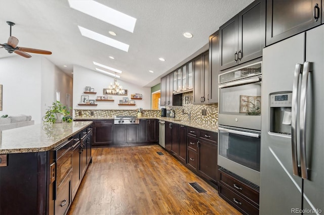 kitchen featuring vaulted ceiling with skylight, kitchen peninsula, tasteful backsplash, wood-type flooring, and stainless steel appliances