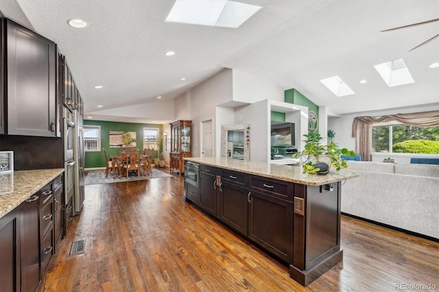 kitchen with light stone counters, a kitchen island, dark brown cabinets, vaulted ceiling, and dark hardwood / wood-style flooring