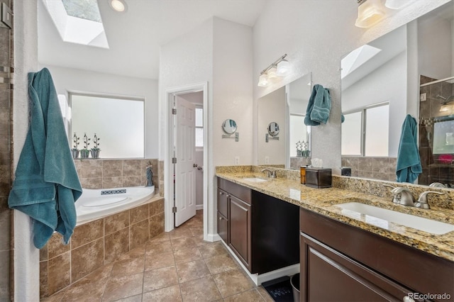 bathroom with tile patterned flooring, tiled bath, a skylight, and vanity