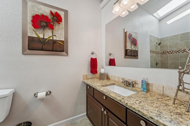 bathroom featuring a skylight, toilet, a tile shower, tile patterned floors, and vanity