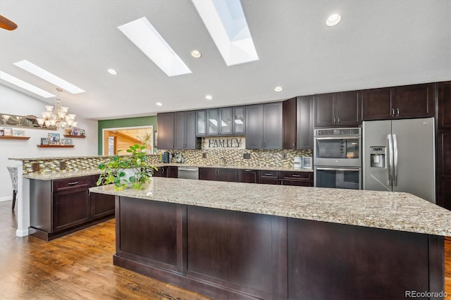 kitchen with appliances with stainless steel finishes, a kitchen island, hardwood / wood-style floors, and light stone counters