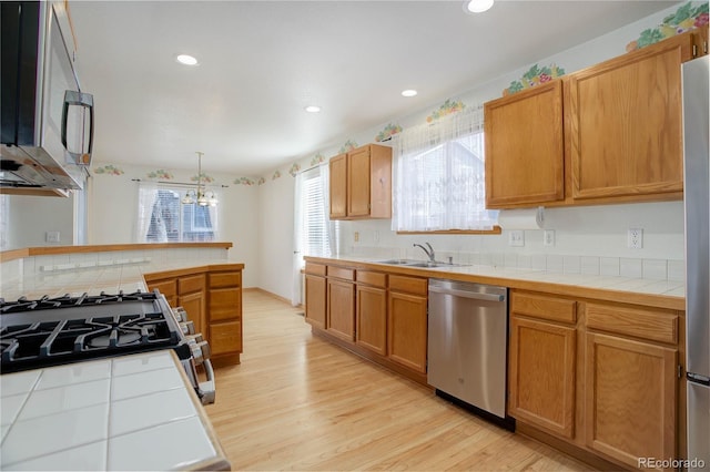 kitchen with decorative light fixtures, stainless steel appliances, sink, tile countertops, and light hardwood / wood-style flooring