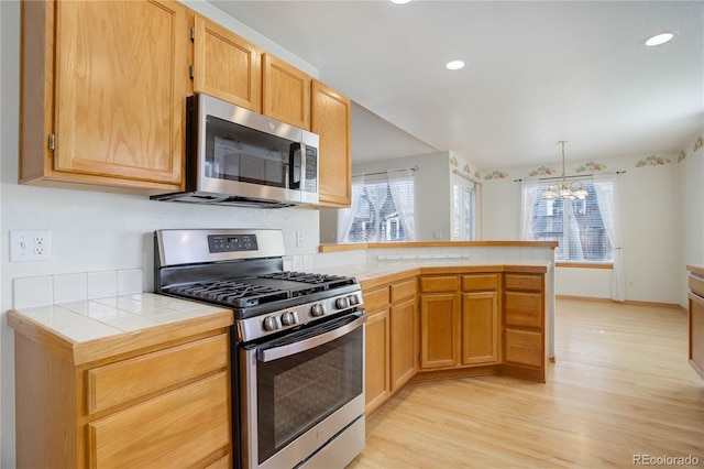 kitchen with kitchen peninsula, appliances with stainless steel finishes, light hardwood / wood-style floors, an inviting chandelier, and tile counters