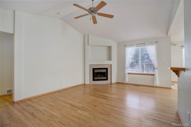 unfurnished living room with a textured ceiling, vaulted ceiling, ceiling fan, light hardwood / wood-style flooring, and a tiled fireplace